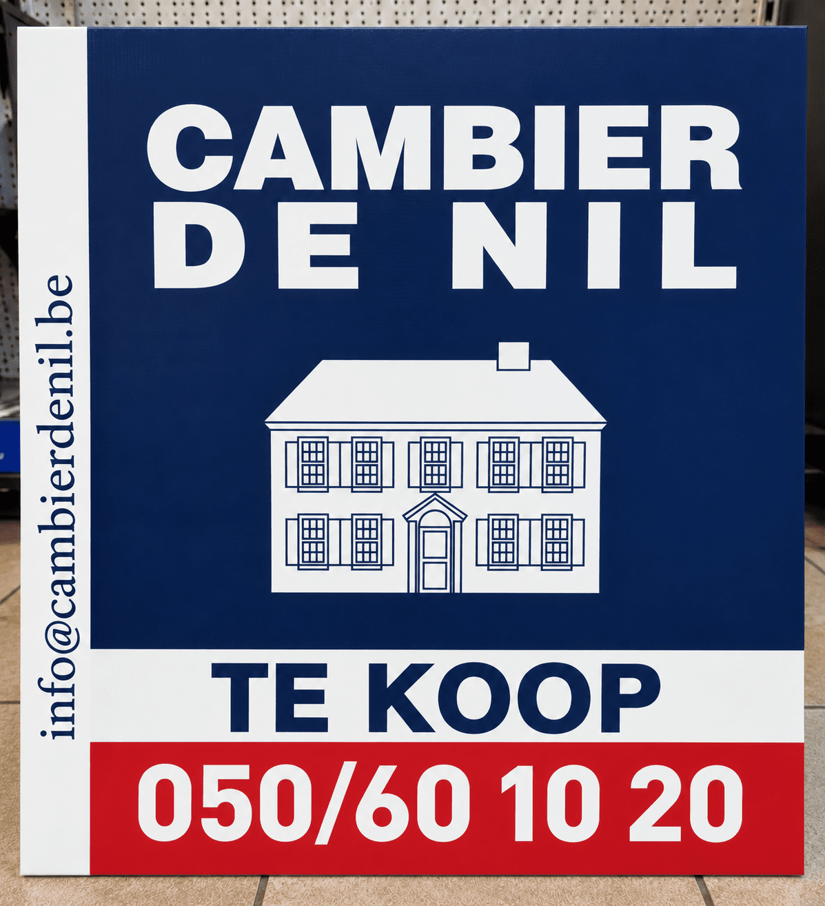 Professioneel immobord 'Te Koop' voor vastgoedkantoor Cambier De Nil, met donkerblauwe achtergrond, witte belettering en rode contactstrook. Voorbeeld van vastgoeddrukwerk op maat door Idee Fiks Printing.